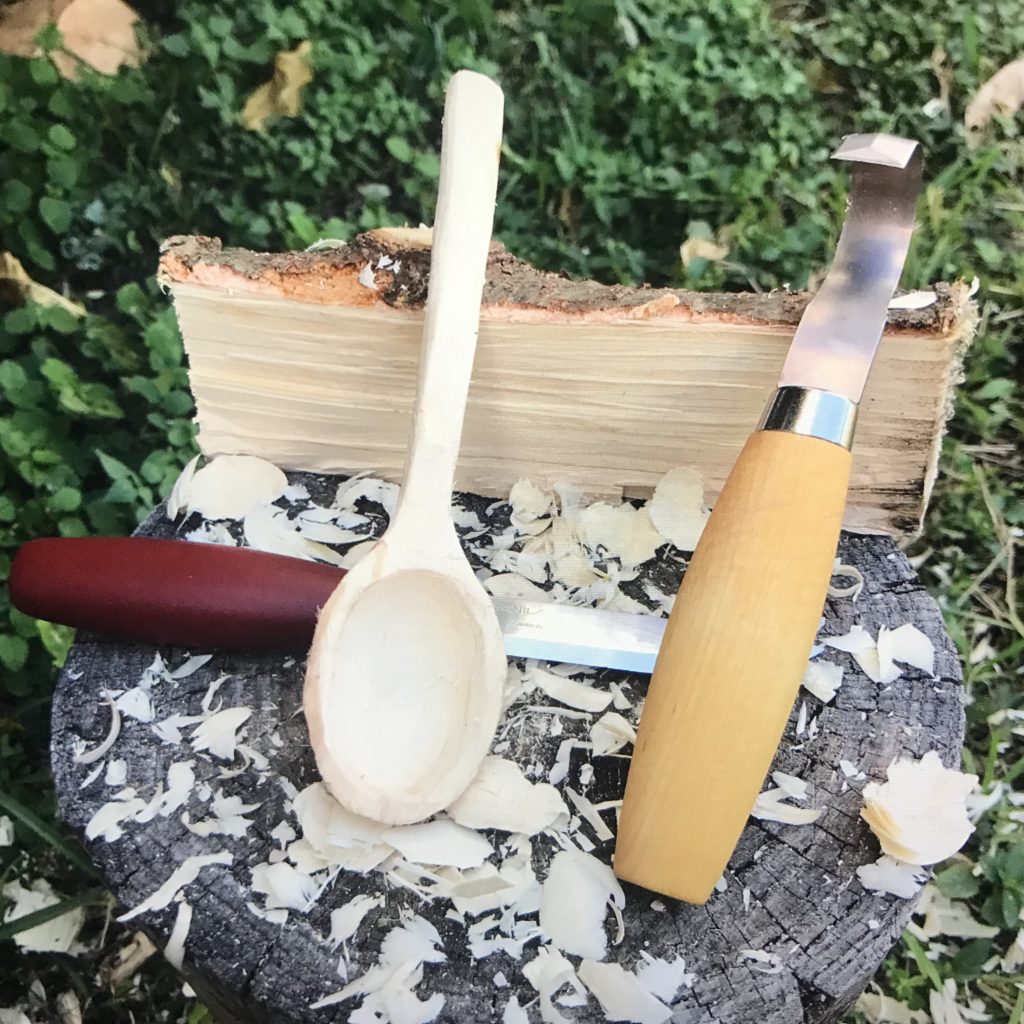 A wood spoon leaning against a split log along with two carving knives
