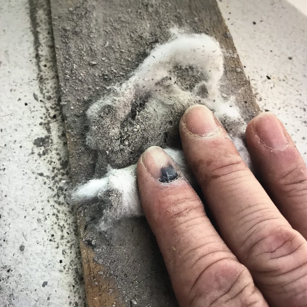 A flat hand rolling a cotton ball covered with wood ash