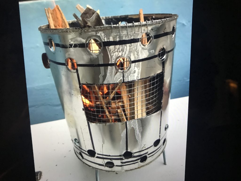 A paint can stove on legs full of kindling that has been set on fire