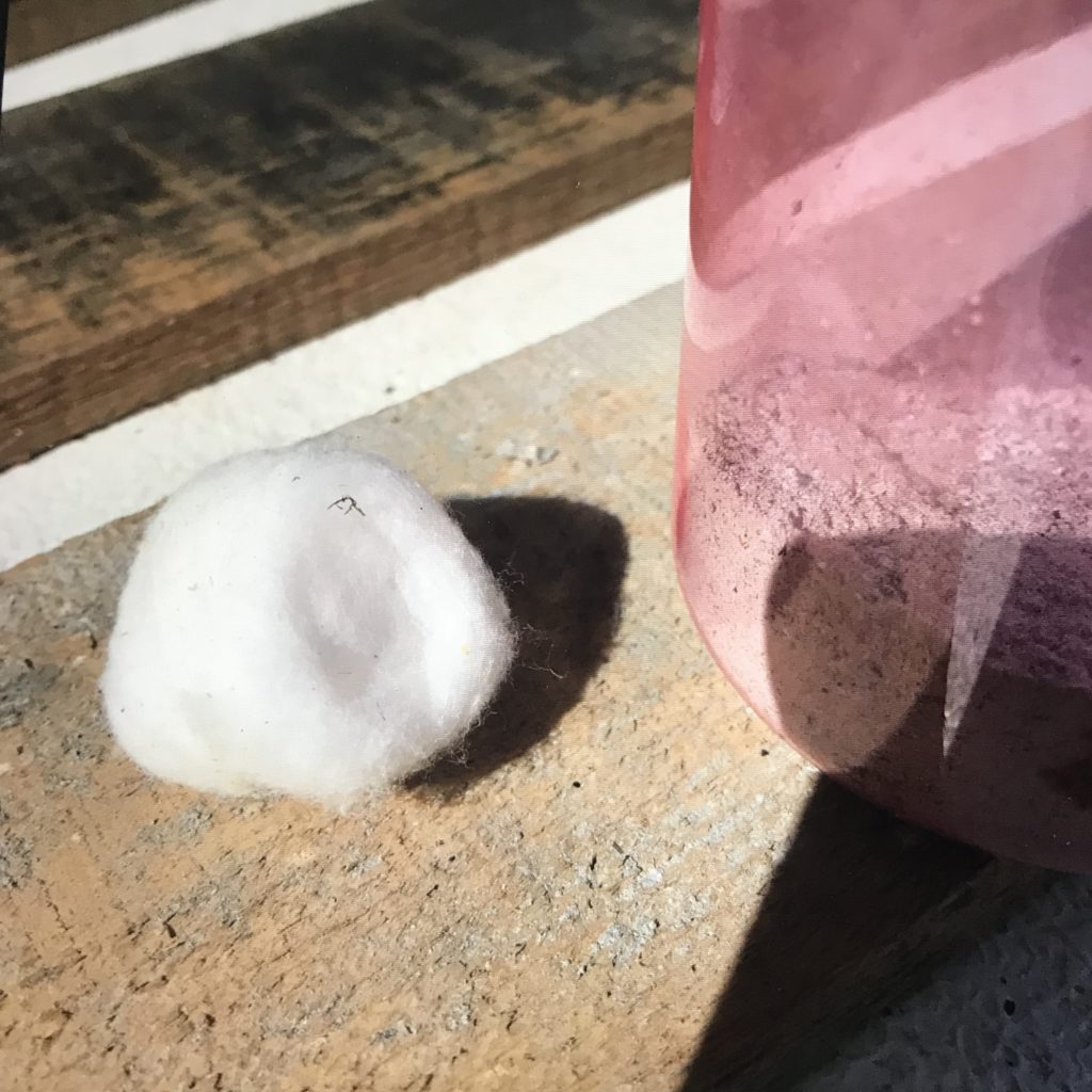 A cotton ball and jar full of wood ash sitting on a wood board