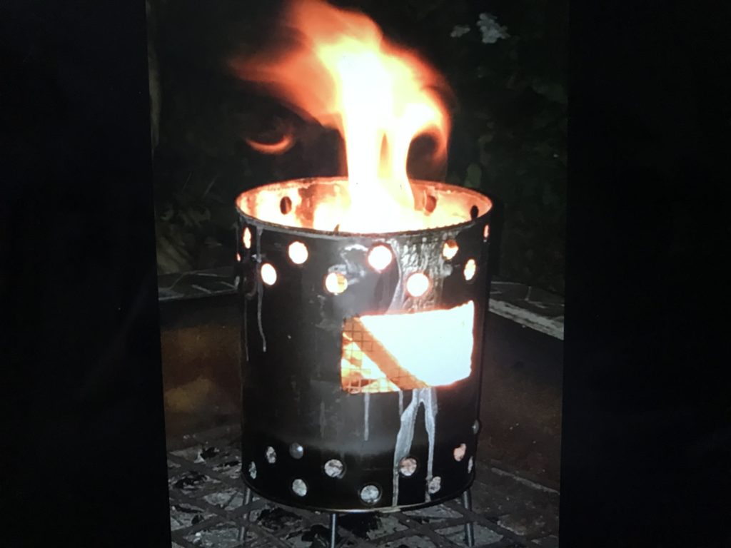 A night shot of a paint can stove blazing with fire