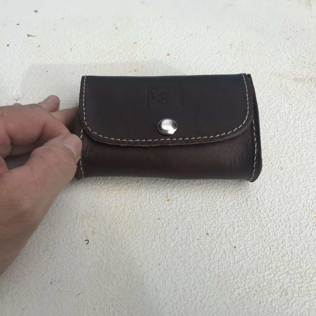 A small wallet sized leather stitched pouch with a persons fignger tips shown for scale
