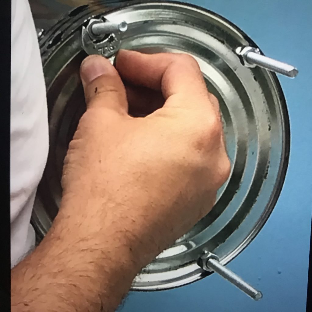 A hand holding a wrench tightening a bolt to the bottom of a metal paint can