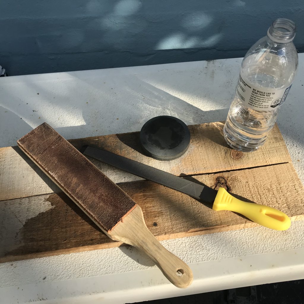 Sharpening tools on a table, file, wet stone, water and a leather strope.