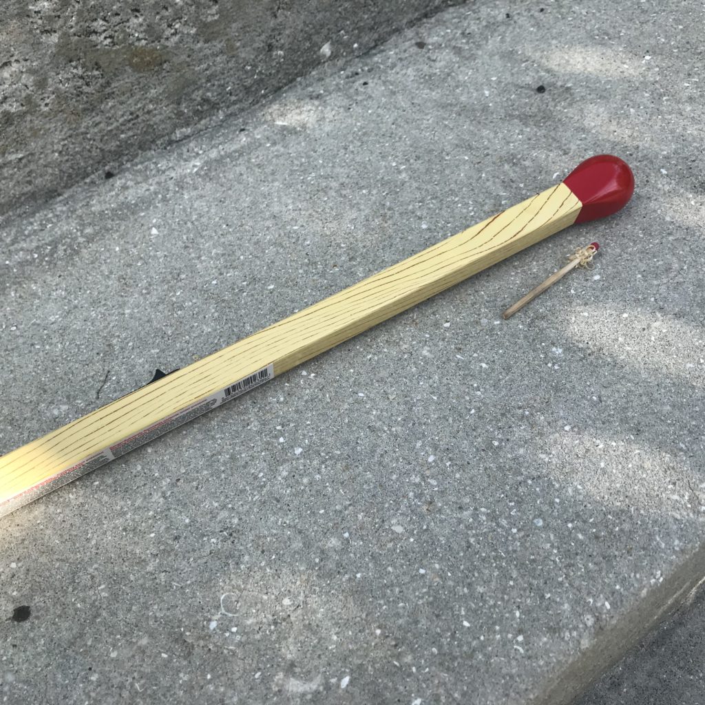 A large butane matchstick lighter alongside a small wood matchstick that has been feathered