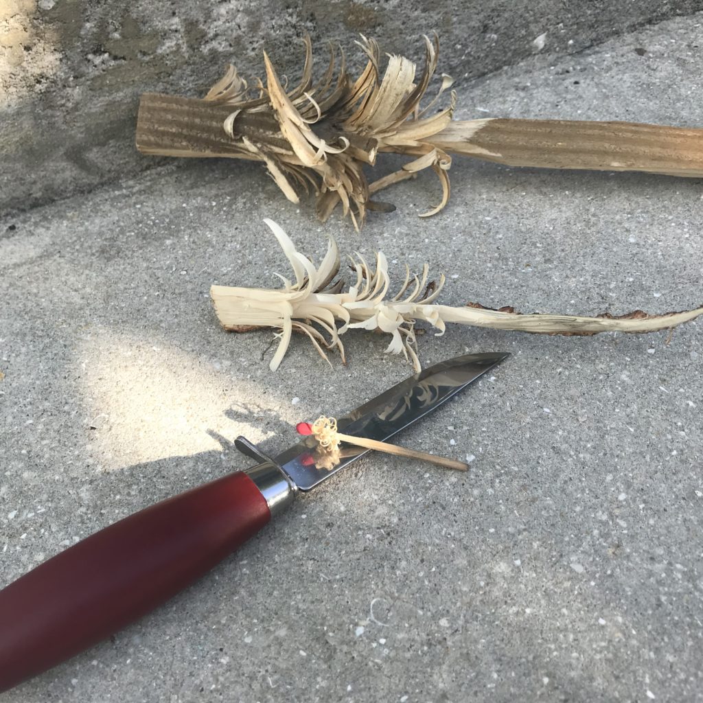 Three different feather sticks and a knife on concrete